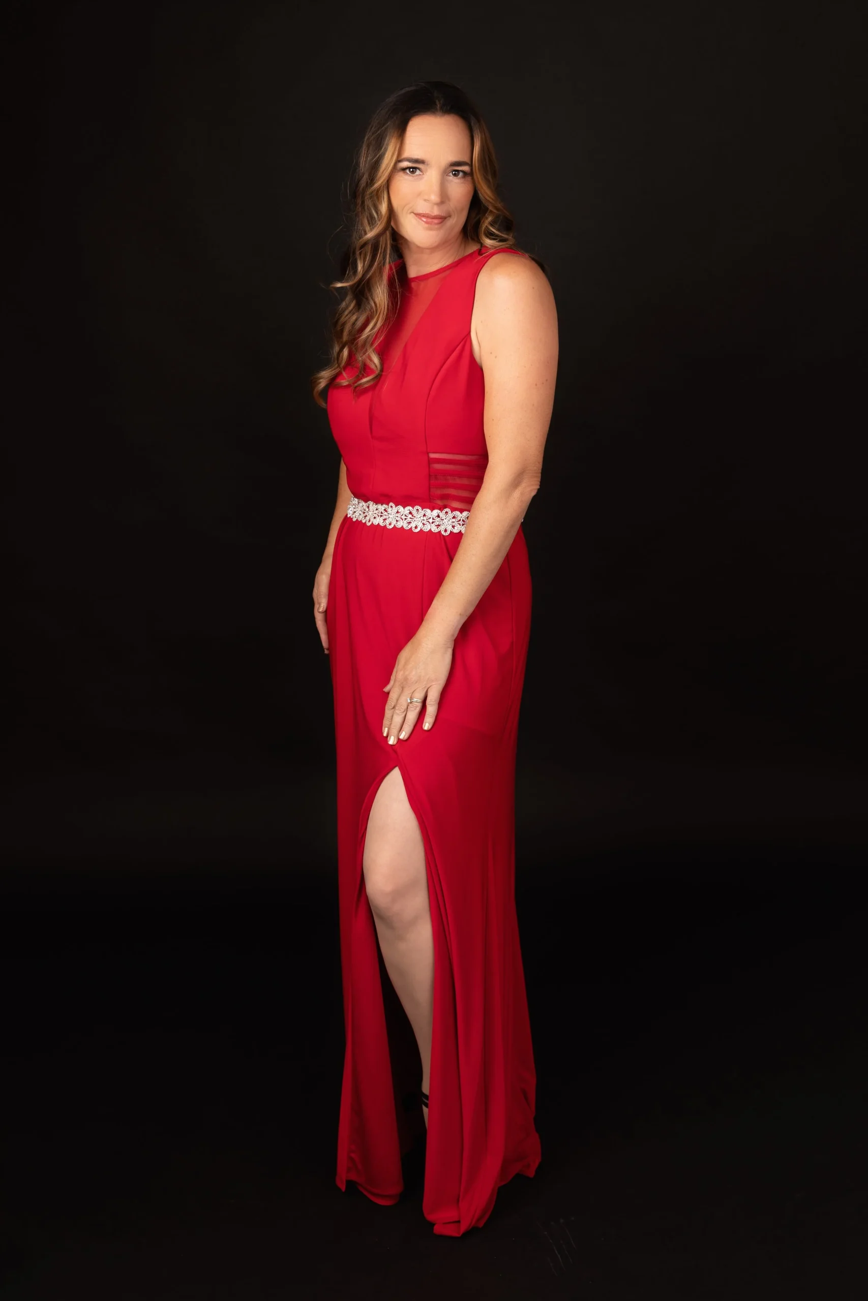 Woman in a red evening gown with a slit, posing against a black background.