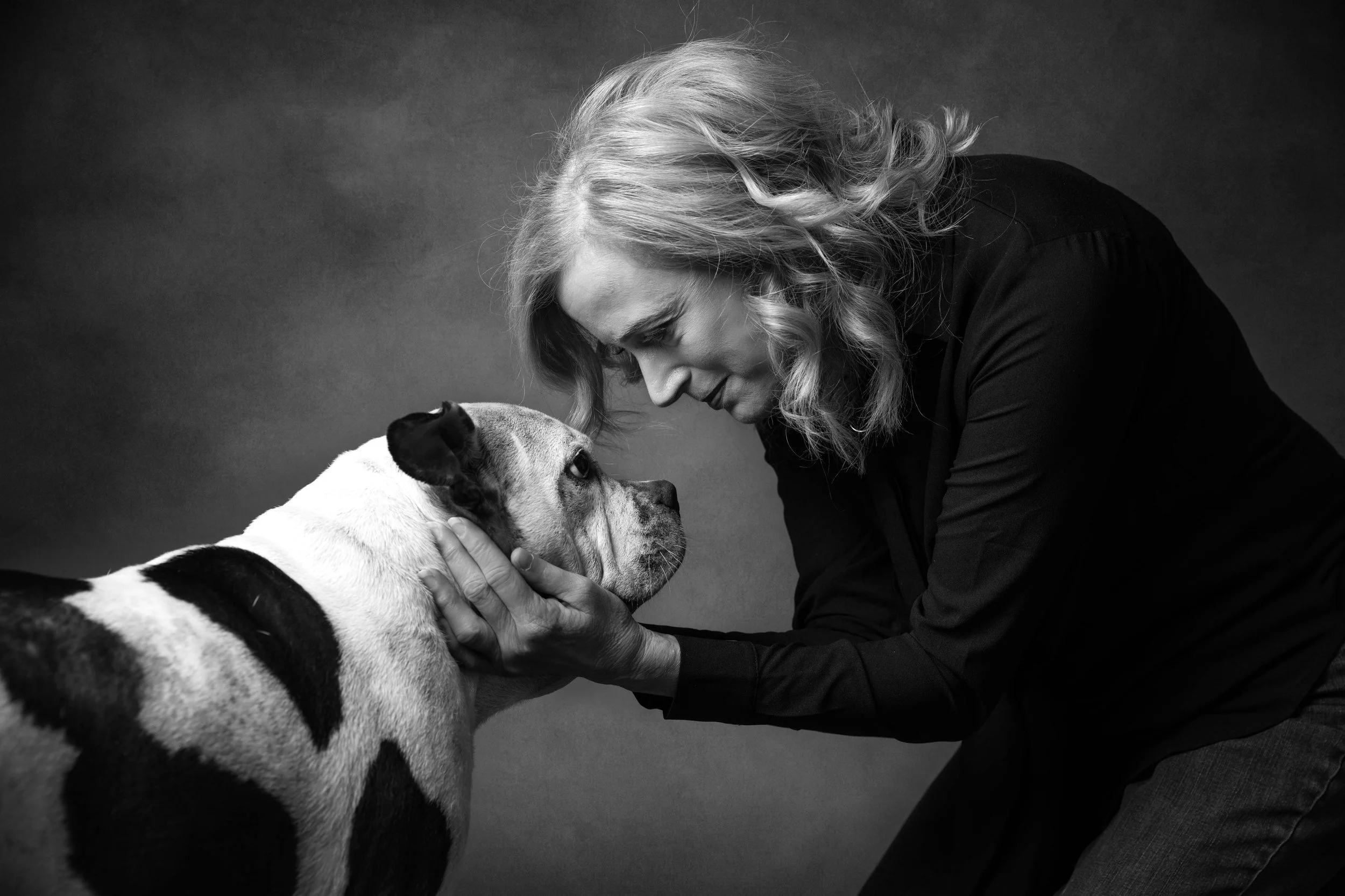A woman gently holds a dog's face, both gazing into each other's eyes in a black and white photo.