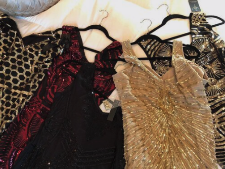 Several dresses with intricate gold, black, red, and beige designs hanging on black hangers.